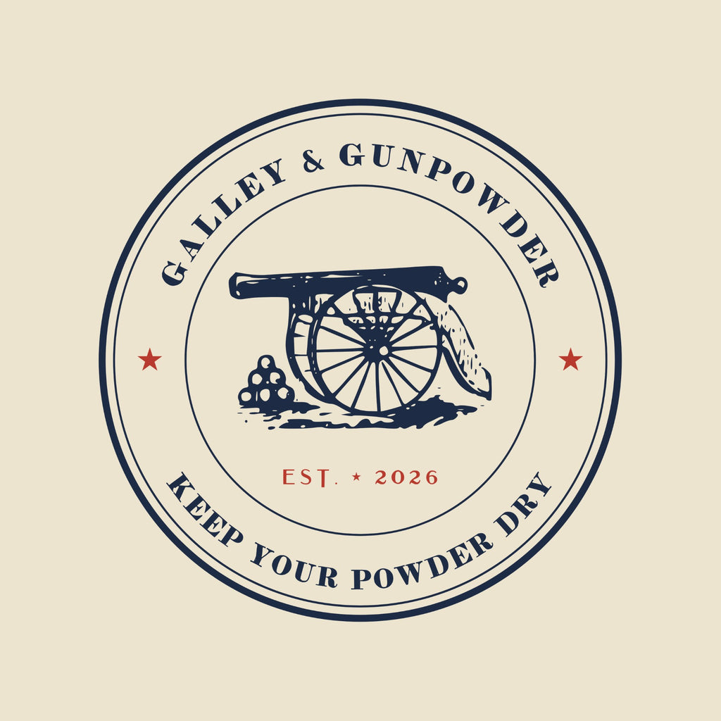 A round seal with GALLEY & GUNPOWDER arched across the top and KEEP YOUR POWDER DRY around the bottom, two red stars, and at its centre an engraving of a field gun beside a pile of cannonballs, with EST. 2026 in red.