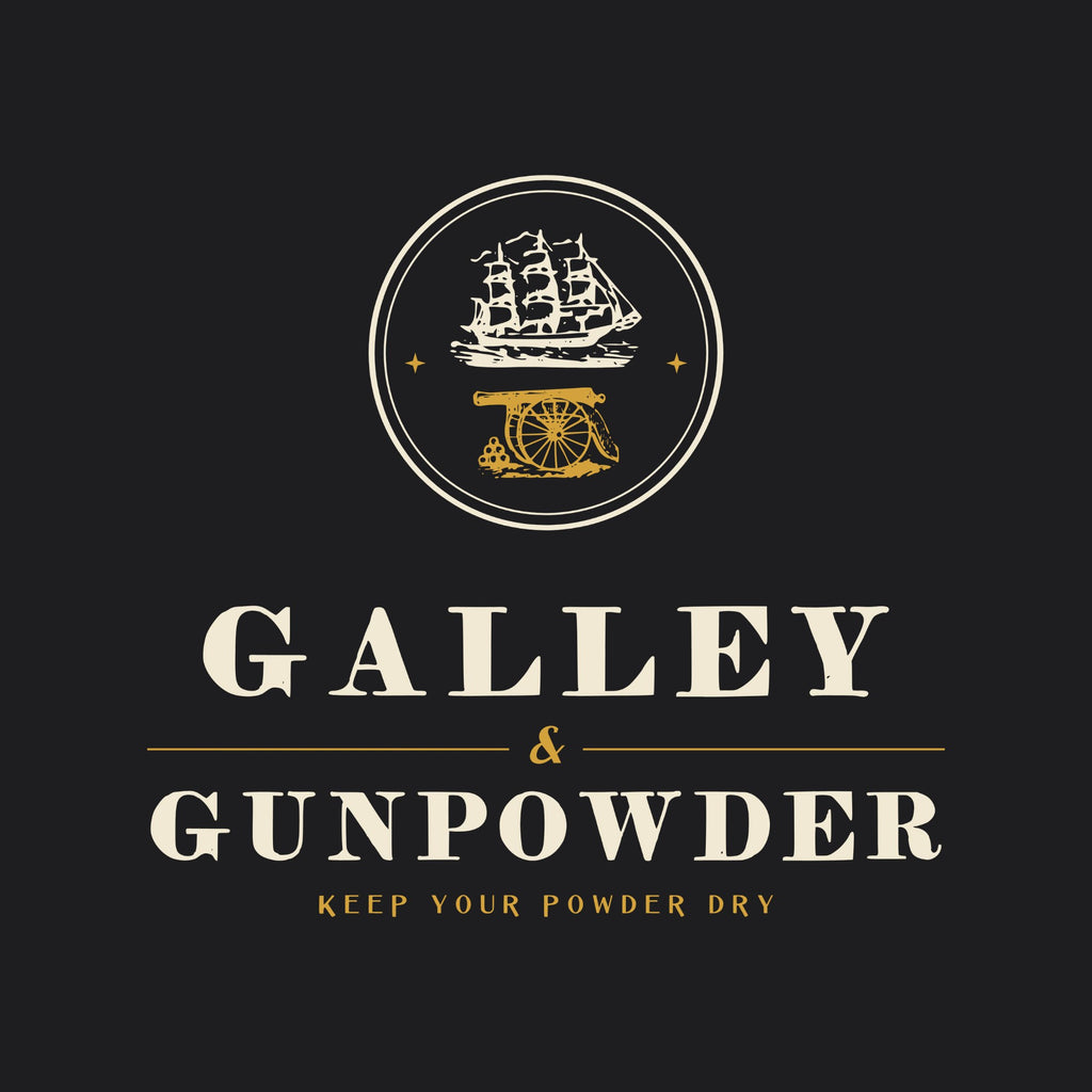 A double ring holding a three-masted ship over a field gun and a pile of cannonballs, with two small brass stars, above GALLEY & GUNPOWDER split by a ruled ampersand and KEEP YOUR POWDER DRY.